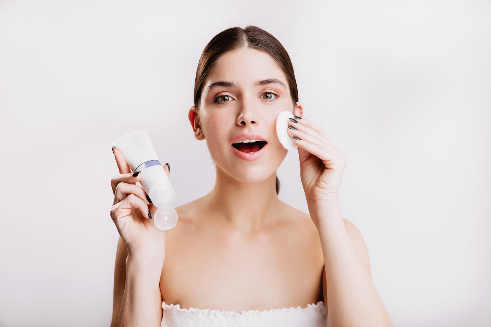 close up shot of green eyed girl doing spa procedure on white background. woman moistens her face with dove cream.